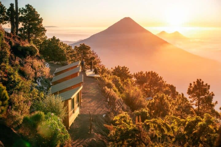 Sunrise casting golden light over OX Expeditions cabins at Acatenango campsite with Agua volcano and Pacaya volcano in the background