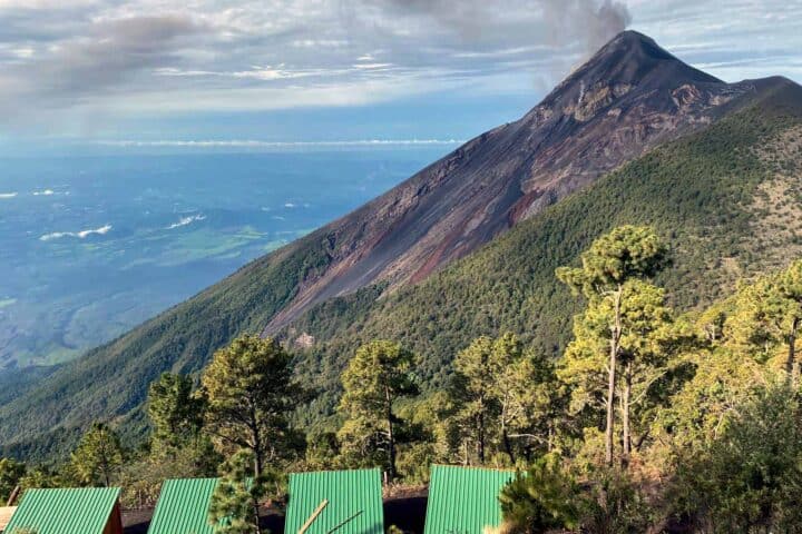 Panoramic view of Fuego volcano rising above forest in front of OX Expeditions cabins at Acatenango campsite