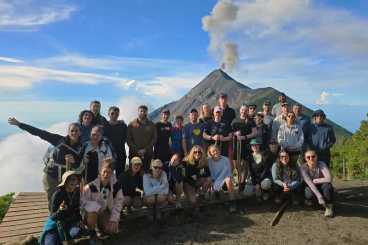 Group of hikers at OX Expeditions Acatenango campsite posing with erupting Fuego volcano in the background
