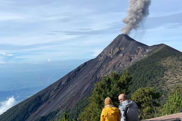 Two hikers seated on campsite platform watching an eruption of Fuego volcano from Acatenango