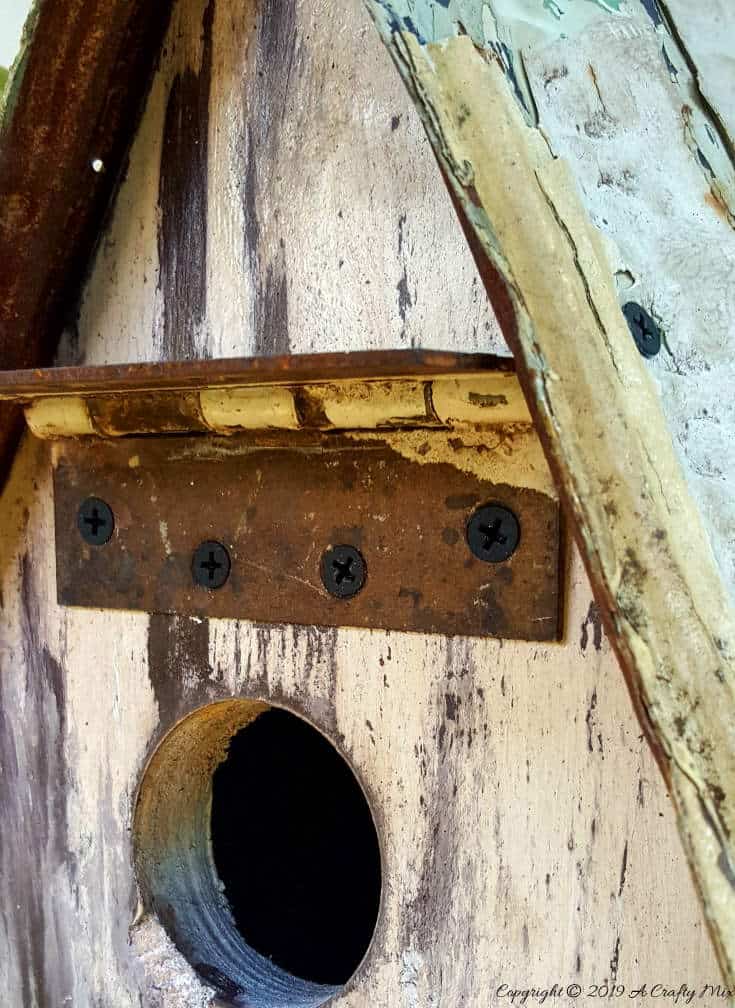 A rusty hinge for an awning. Want to add some rusty curb appeal or improve your backyard? This cute and wacky birdhouse is made entirely from recycled bits and has so much character. It’s inexpensive and easy to make too The tutorial includes all the instructions to make your own. #rusticbirdhouse #DIYbirdhouse #paintedbirdhouse #acraftymix #birdhouseideas #uniquebirdhouse