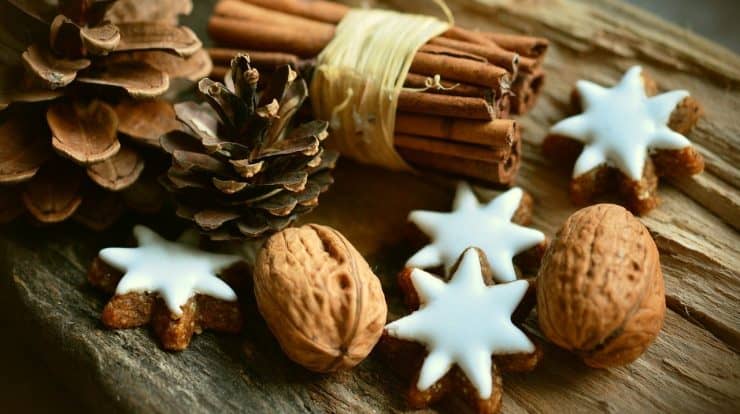 Sprigs of cinnamon, star-shaped cookies with white icing, walnuts, and pinecones arranged on rustic wooden surface for holiday or winter celebration.