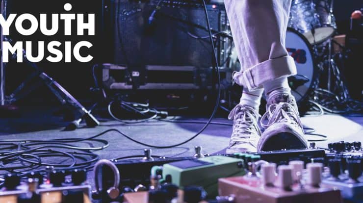 Performing youth musician on stage with guitar effects pedals and sound equipment, emphasizing youth music, live performance, and musical creativity for youth music enthusiasts.