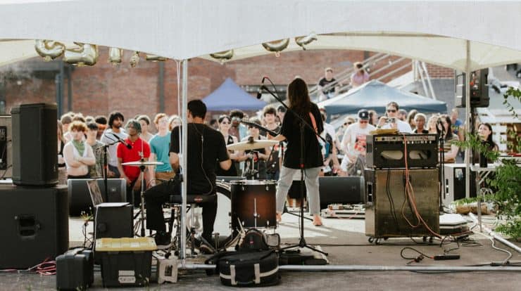 Live outdoor concert performance at a music festival with band playing under a tent, audience enjoying the music, vibrant atmosphere, and sound equipment setup.