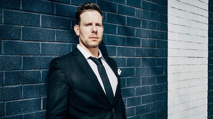 Professional businessman in a tailored suit standing against a modern brick wall, representing insights on the music industry, digital marketing, and entrepreneurship themes on Hypebot.