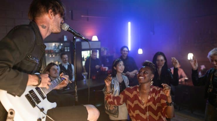 Live music performance at a vibrant nightclub with an enthusiastic audience enjoying the artist's guitar and singing, creating a lively and energetic atmosphere.