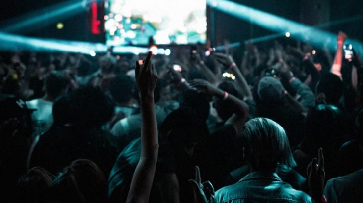 Vibrant concert crowd at a live music event with hands raised, colorful lights, and energetic atmosphere, capturing the essence of music festivals and nightlife entertainment.
