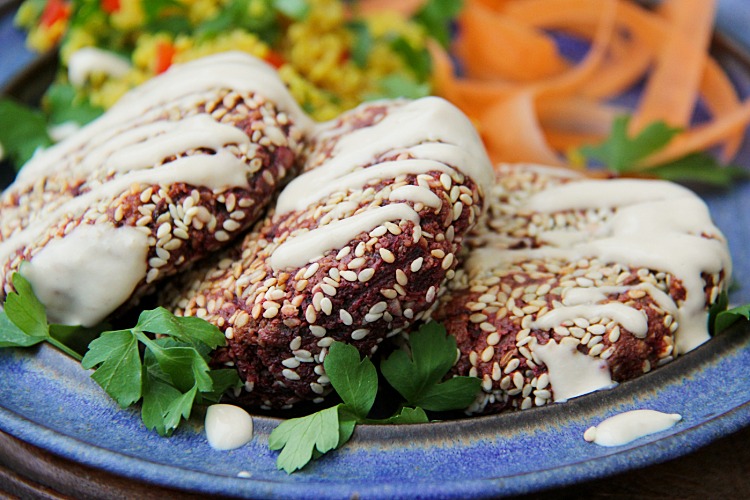 Beetroot burgers on a plate with tahini sauce and salad