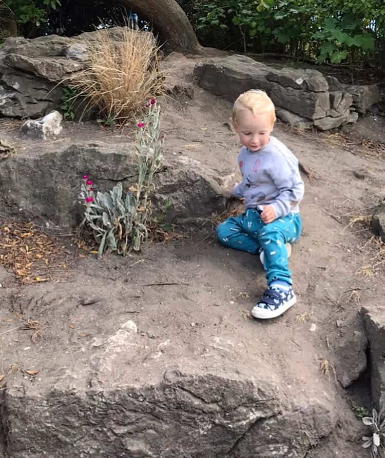 William wearing soft trousers and a jumper sitting on an earthy bank
