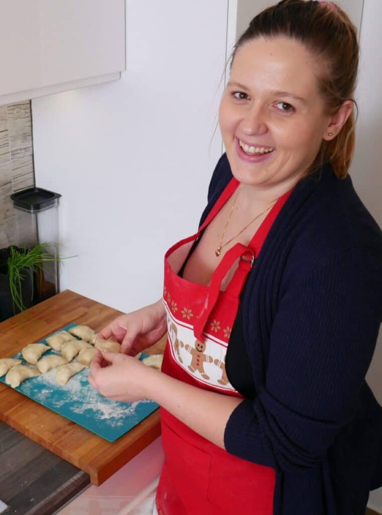 A woman in a red apron is preparing Polish dumplings.