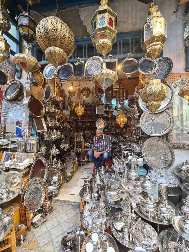 A vendor surrounded by ornate silver lanterns and trays at a market in the medina of Tunis