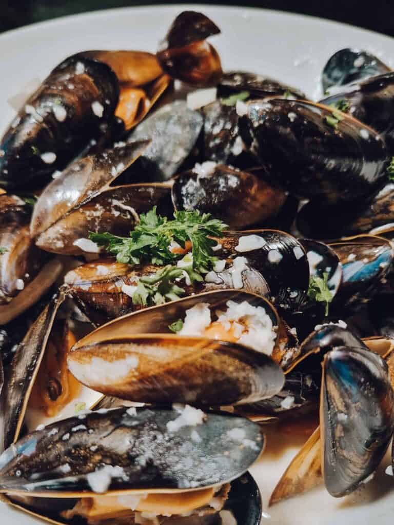 A close-up of a plate of steamed mussels garnished with chopped herbs and garlic, served in their shells.