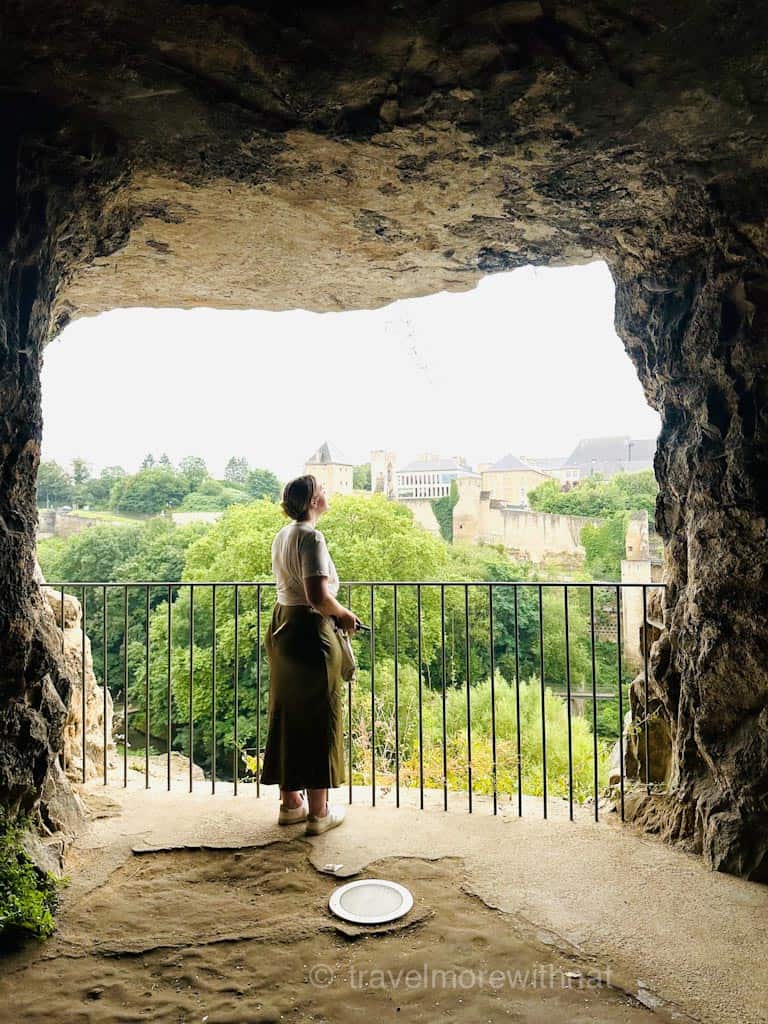 A woman standing on a balcony overlooking a city, framed by a cave opening. Travelling with ADHD doesn't stop her enjoying her trips.