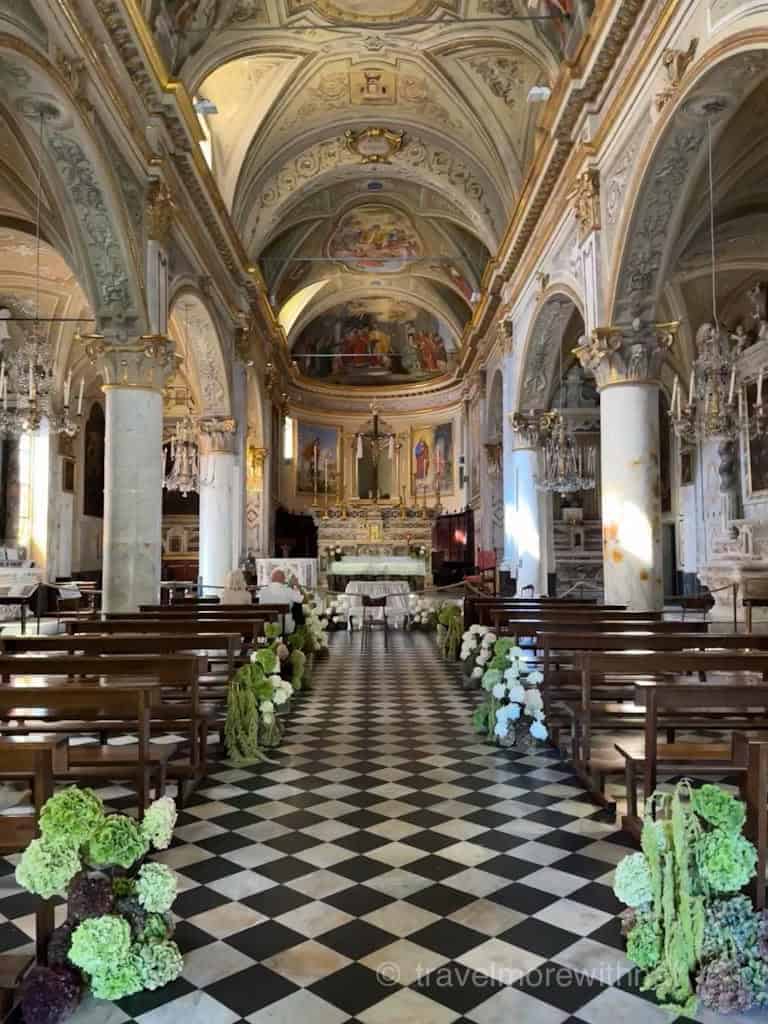 An ornate church interior with a decorated aisle, rows of wooden pews, and a checkered floor. Chiesa del Divo Martino decorated for a wedding day in Portofino.
