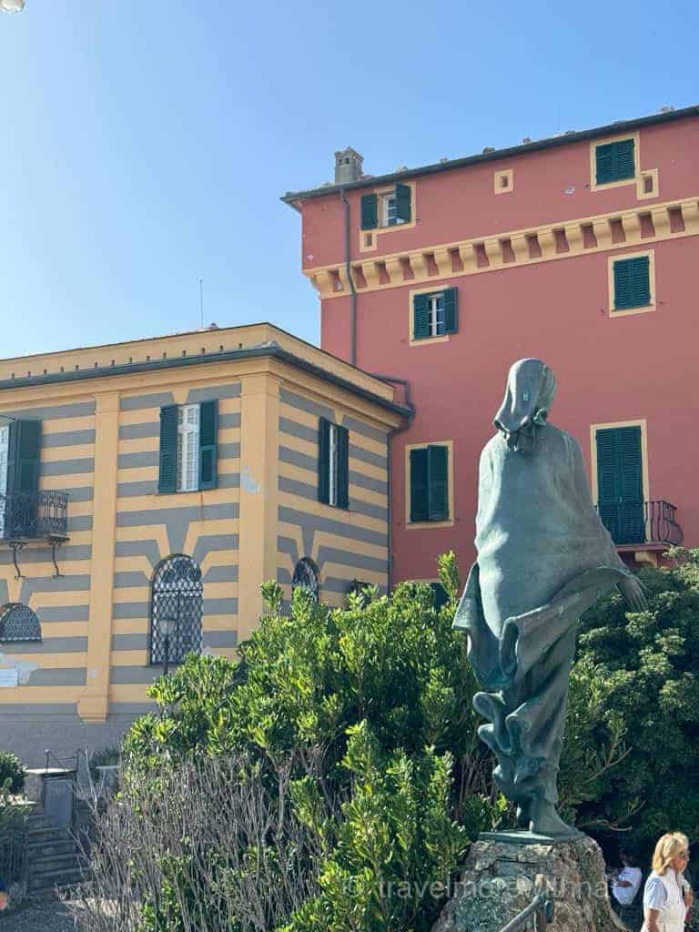 Colourful buildings with striped facades and a bronze statue of a woman in a piazza outside Chiesa di San Giorgio in Portofino.