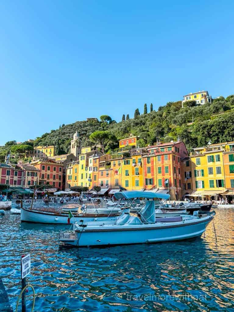 Colourful buildings lining a harbour with boats, nestled on a hillside overlooking the water. The perfect stop during a day in Portofino.
