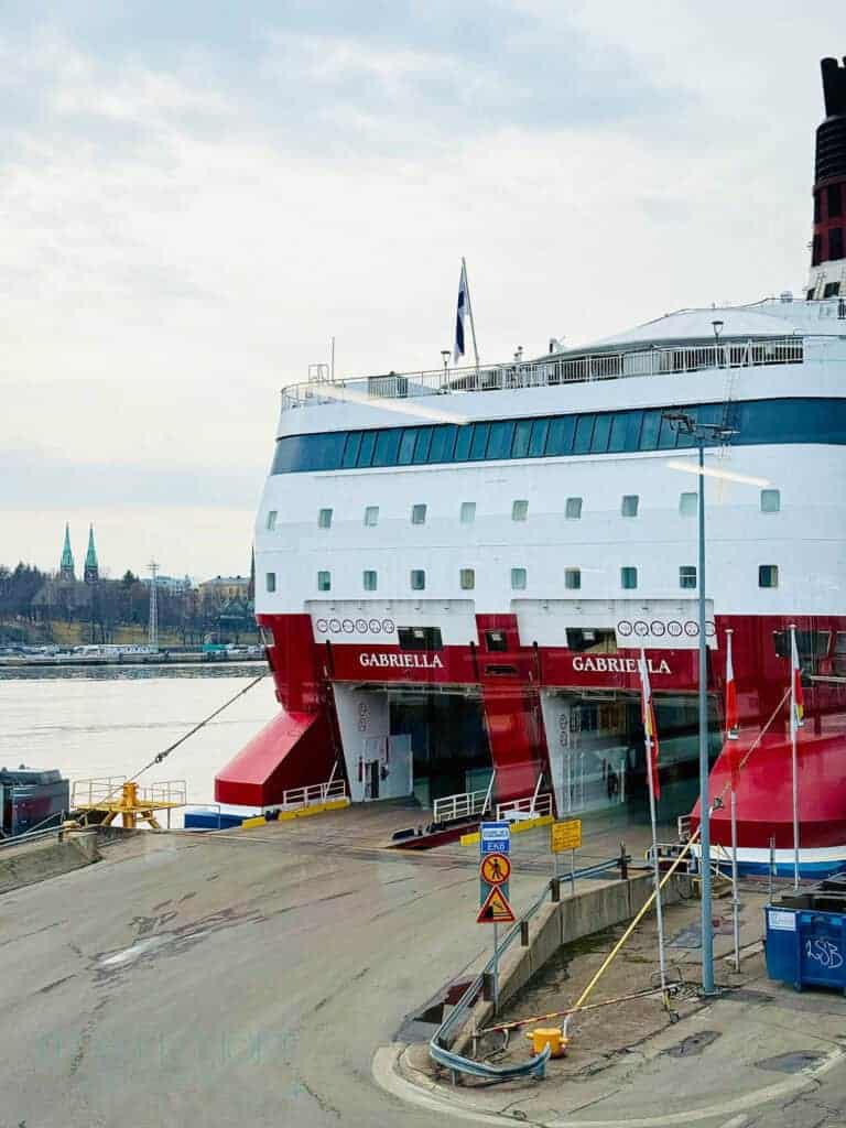 A road leads directly into the car loading level of a large red and white ship, docked on the edge of Helsinki city - the name 'Gabriella' can be seen above the entrances. It's preparing for a ferry crossing to Tallinn.
