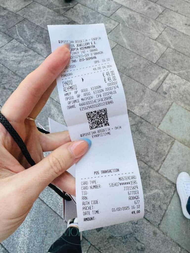 Hand holding a printed receipt in Greek, showing a €49 purchase from a Pandora shop in Athens. Receipts like these are often needed for claims, which won’t be covered if you’re travelling without insurance.