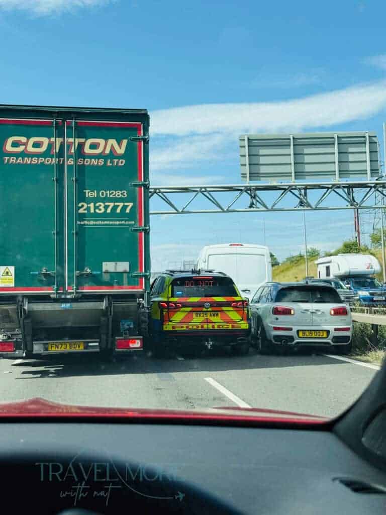 Traffic jam on a motorway showing a green transport truck, a police vehicle, and a small car in close quarters. Travel disruptions like this are common, and not having insurance can mean paying out of pocket for delays or accidents.