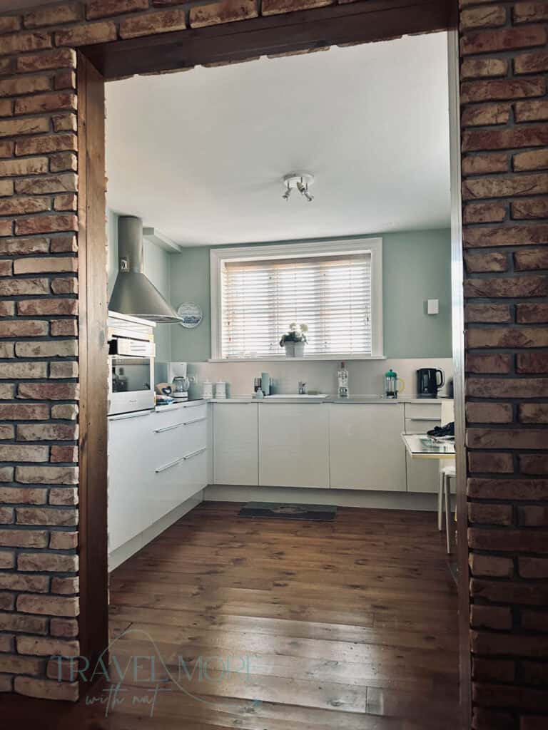A modern kitchen, as seen through a brick archway, with wooden flooring, mint green walls and white cupboards. A kitchen is a bonus when looking for accommodation near Reykyavik.