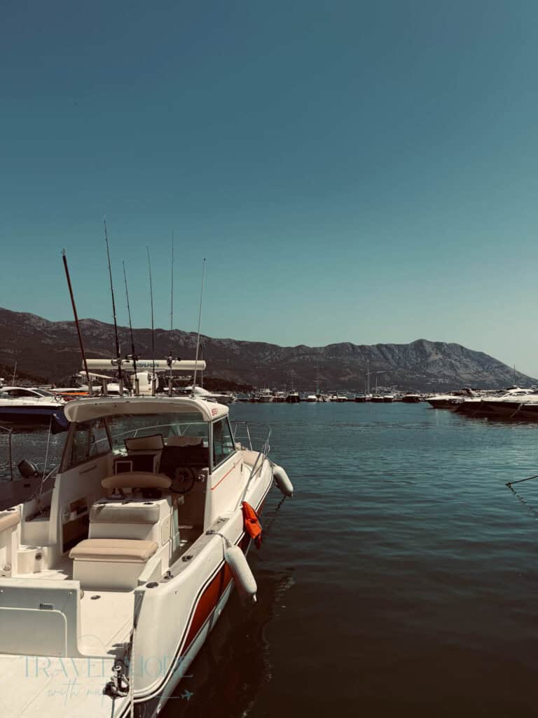 White motorboat with fishing rods docked in a marina filled with yachts, with mountains in the distance — A scenic harbor view and a top pick for what to see in Budva for boating enthusiasts.
