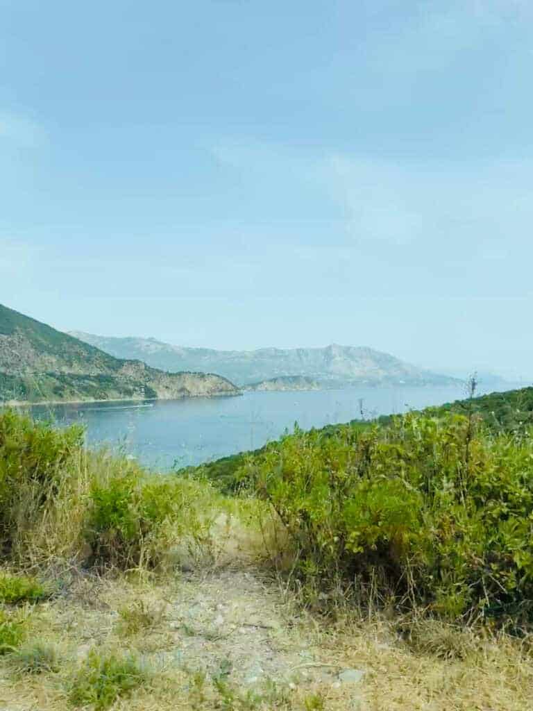 Scenic coastal view from a grassy hilltop showing the blue Adriatic Sea and rugged mountains — A picturesque viewpoint to experience on a hike and one of the best what to see in Budva experiences.