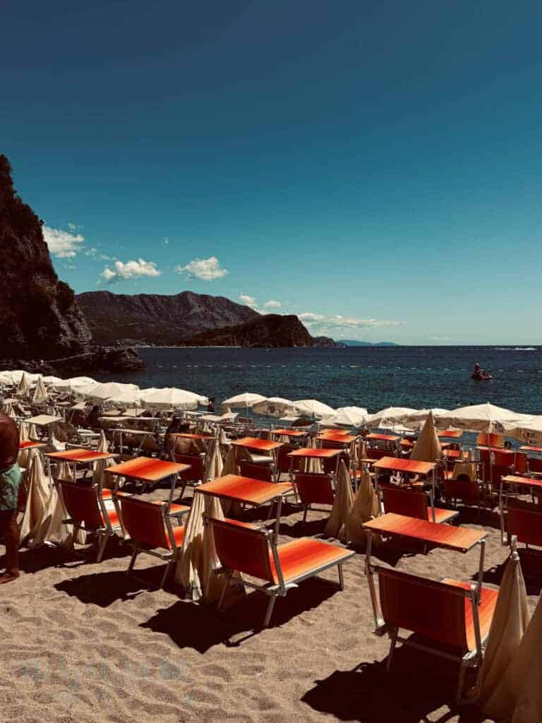 Beach in Budva with rows of bright orange sunbeds and white umbrellas facing the Adriatic Sea — A vibrant seaside spot on the what to see in Budva list.