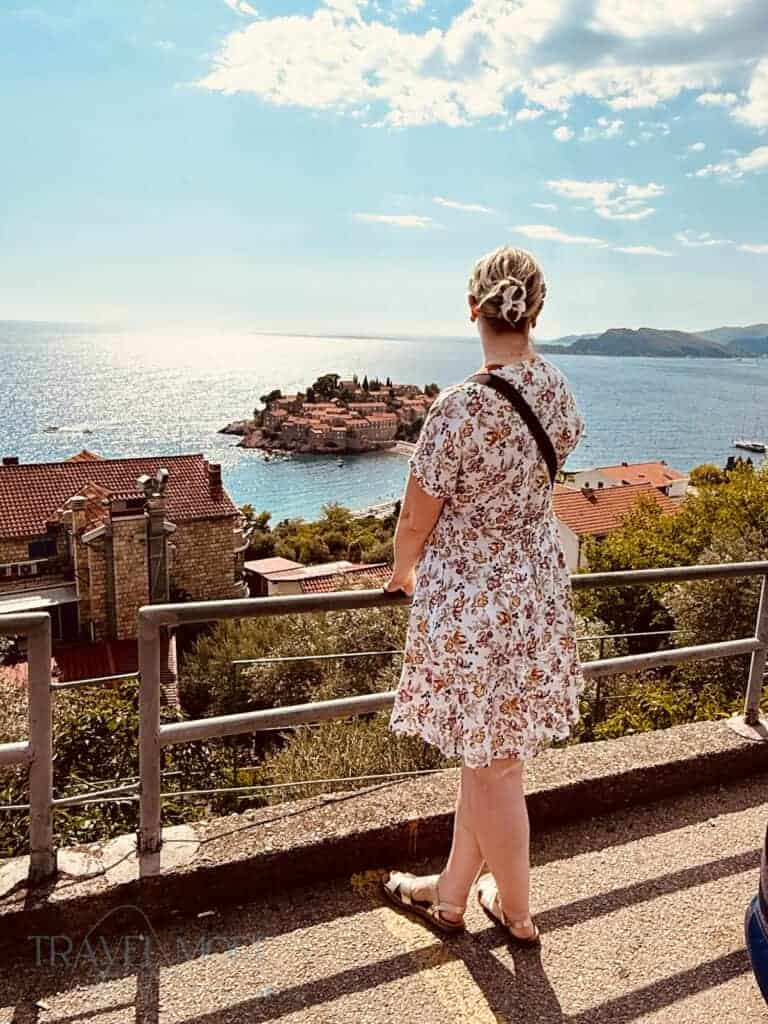 Woman in a floral dress standing at a viewpoint overlooking Sveti Stefan island and the Adriatic Sea — A breathtaking stop when deciding what to see in Budva.