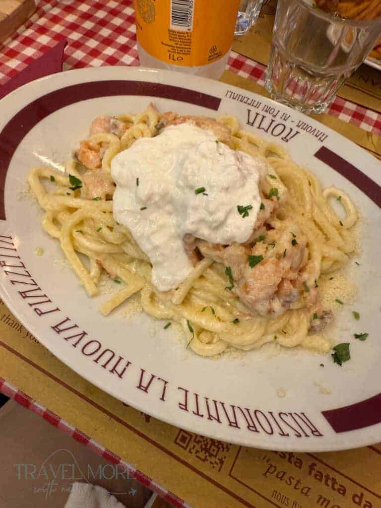 Plate of creamy pasta topped with burrata cheese and garnished with herbs, served at Ristorante La Nuova Piazzetta on a red and white checkered tablecloth.