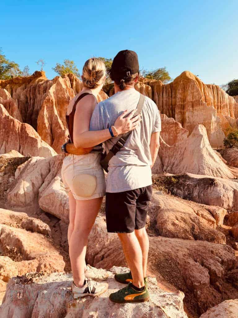 A woman and man stand with their backs to the camera, surrounded by red canyon rocks under a blue sky. A travel planning professional can help customise a bucket list trip like this.