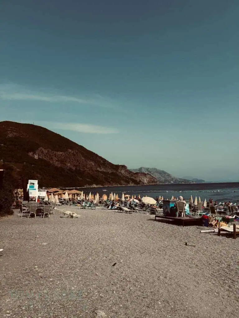 Sun loungers and parasols on one of the best beaches in Budva, beside a rocky bay.