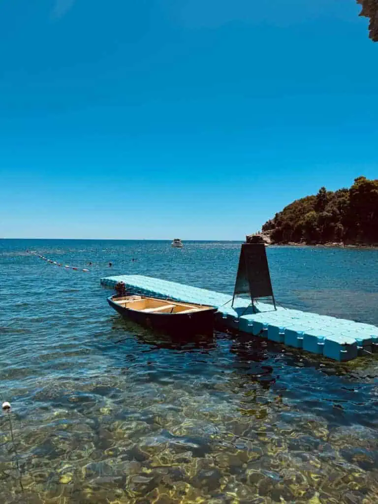 Blue sea, a moored boat, and a floating pier under a cloudless sky in Budva.