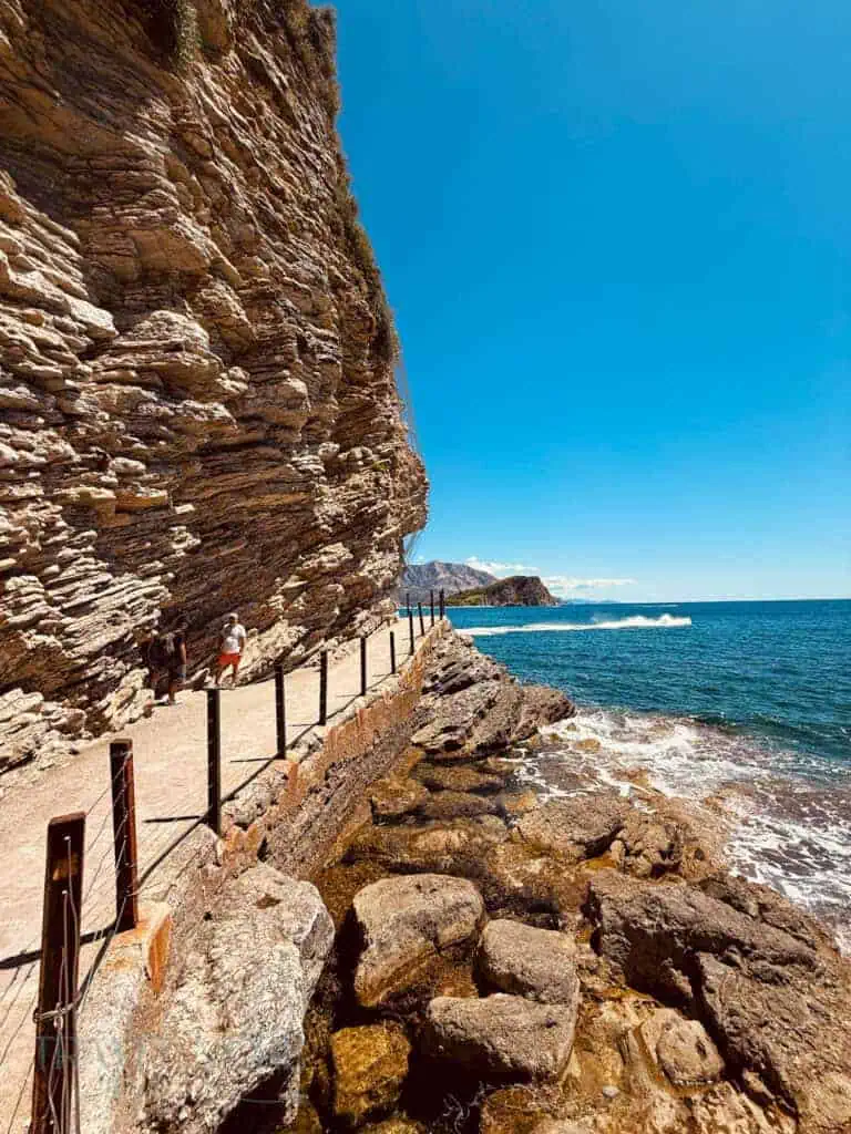Stone path carved into the cliff edge, overlooking rocks, the sea and Budva beaches.