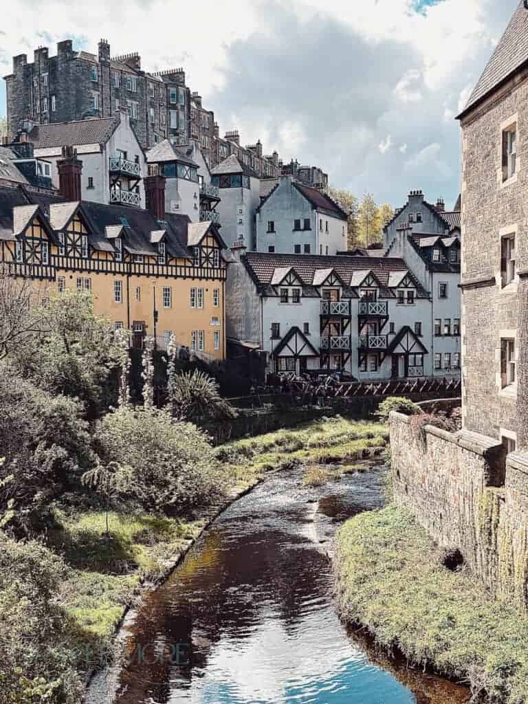 Quaint riverside buildings in Edinburgh’s Dean Village with historic stone apartments rising behind them under a cloudy sky.