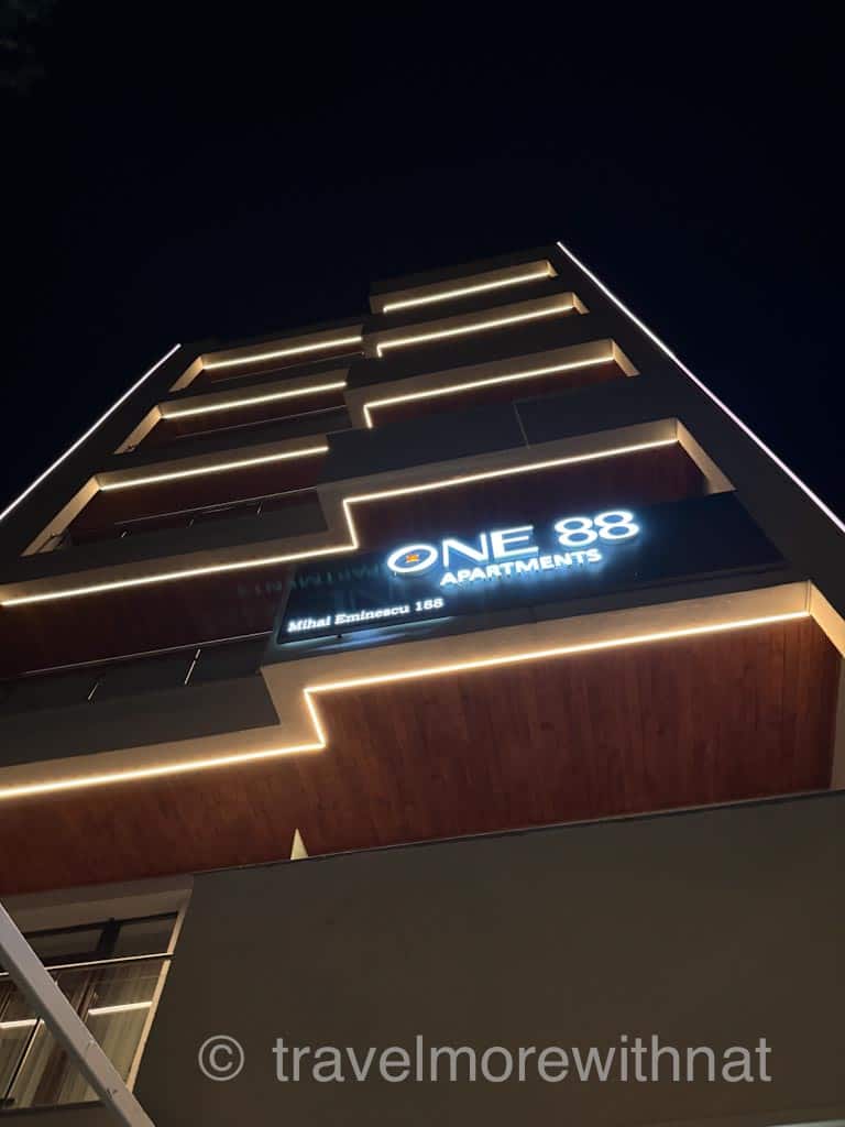 View looking up at the modern and well-lit facade of ONE 88 Apartments in Bucharest, captured at night.