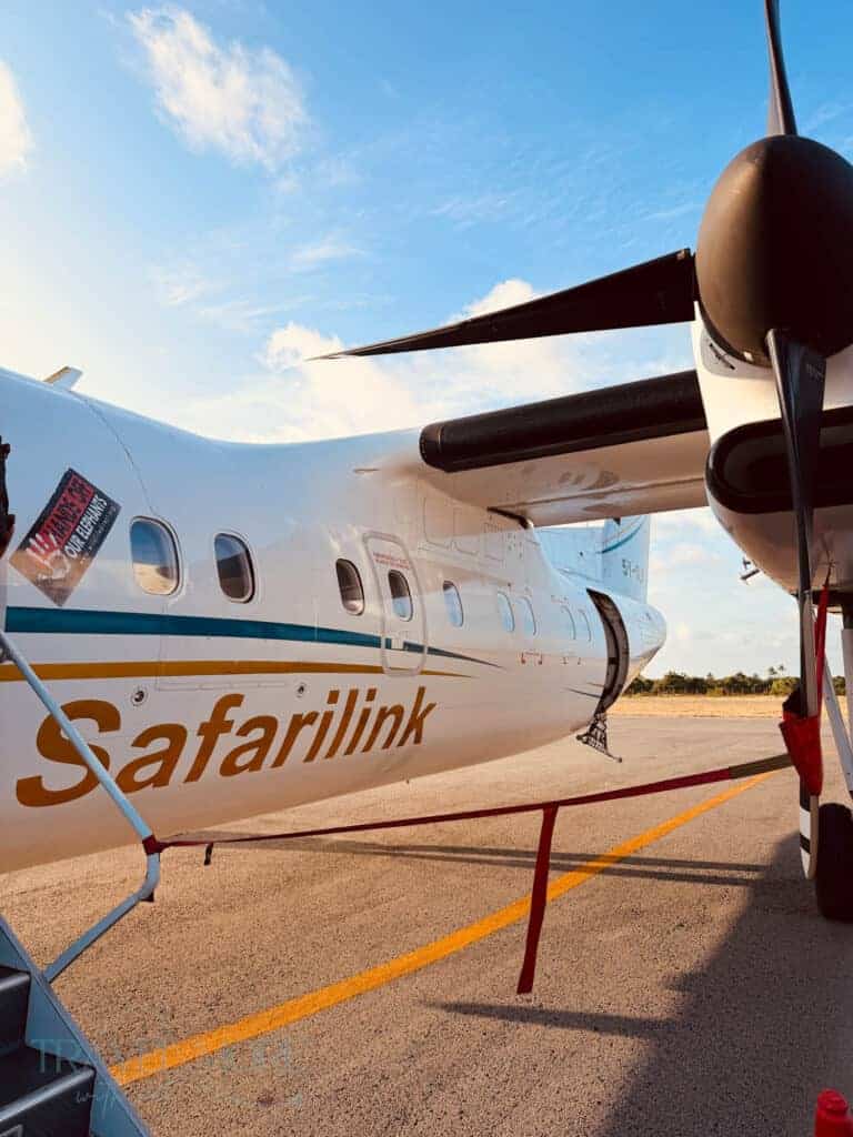 Safarilink turboprop aircraft parked on the airport tarmac under a blue sky with its propeller and fuselage visible. This small regional plane highlights the experience of taking domestic flights Kenya travelers use to reach safari destinations and remote regions across the country.