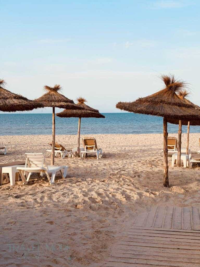 Sandy beach with thatched parasols, white loungers, calm blue sea and a wooden walkway