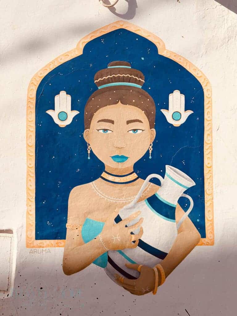 Woman with a high bun holding a large white jug in a colourful mural