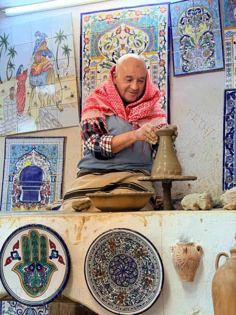 Potter shaping a clay vessel beside decorated ceramic plates