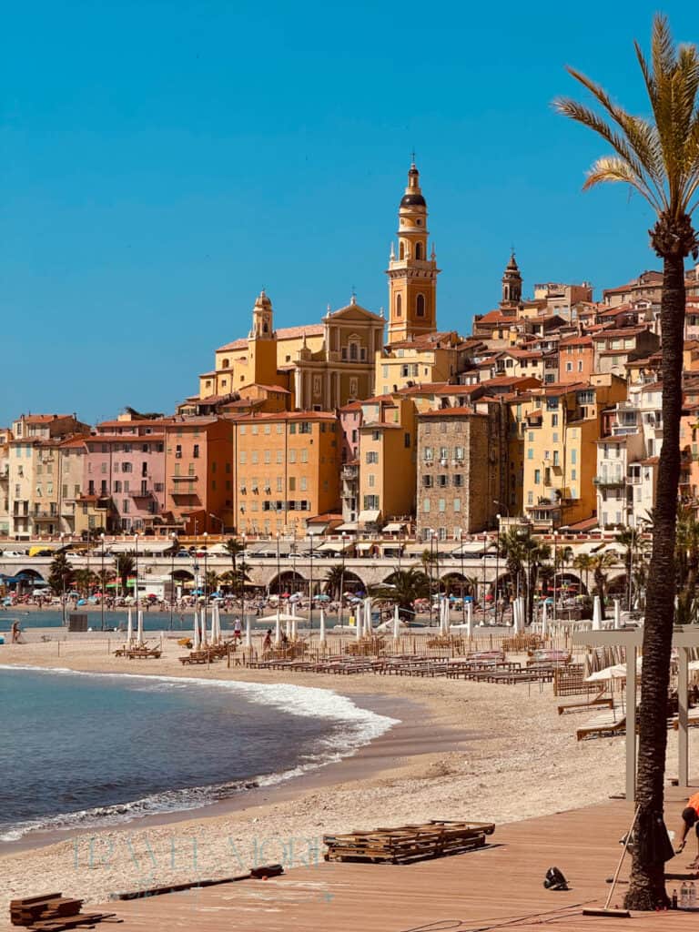 A bright Mediterranean beach view of Menton, with colourful homes climbing the hillside - one of the many things to do in Menton.