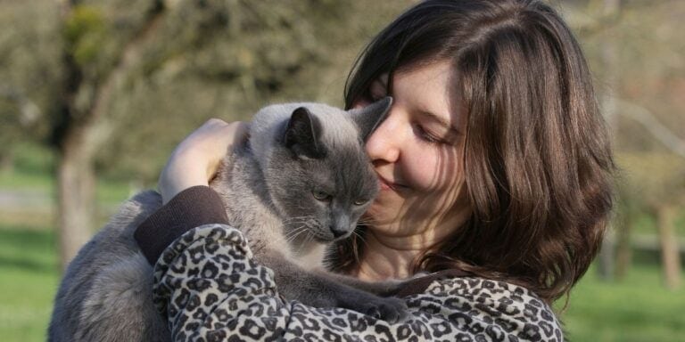 woman in leopard print sweater cuddling her Siamese cat