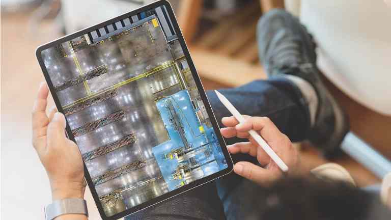 Hands holding an iPad displaying a detailed interior map of a warehouse, used for digital factory layout and facility mapping.