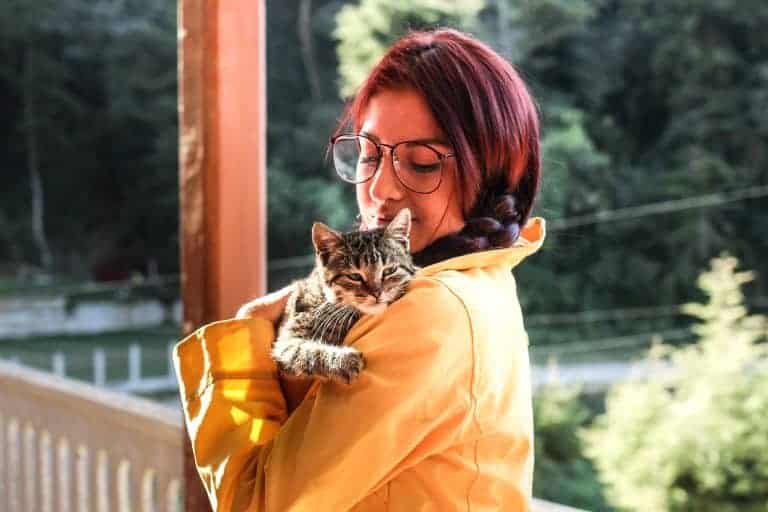 woman in yellow jacket holding a tabby kitten