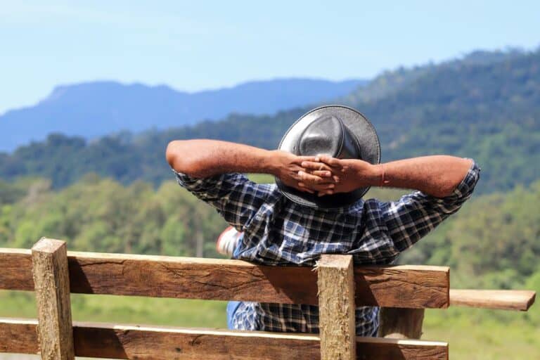 person relaxing on a bench, hands behind head, enjoying a scenic landscape
