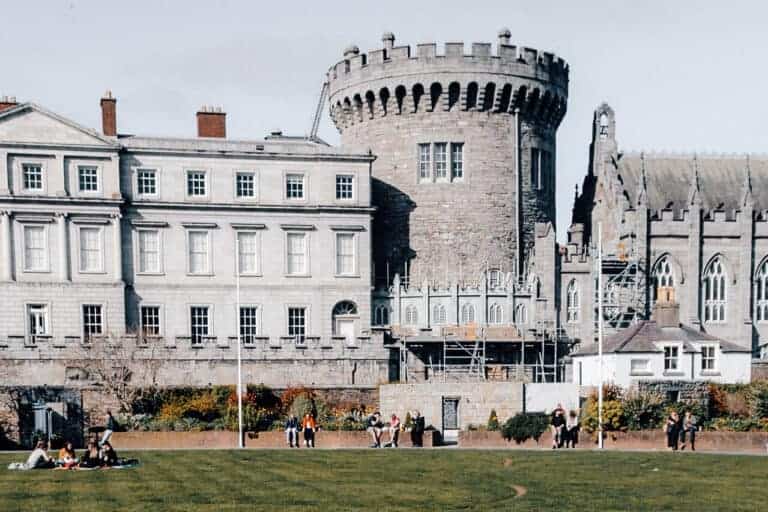 The image shows Dublin Castle, a historic landmark in Dublin, Ireland. The castle's distinctive architecture features a blend of medieval and Georgian styles, with its prominent tower and elegant courtyard surrounded by stone buildings.