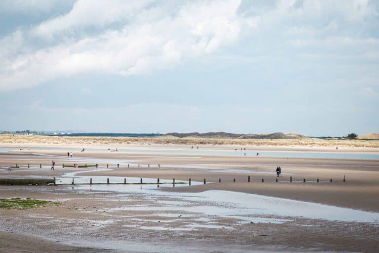 Another view of the coastal walk from Portmanock to Malahide, showcasing sandy paths, grassy dunes, and people walking near the shoreline under a partly cloudy sky.