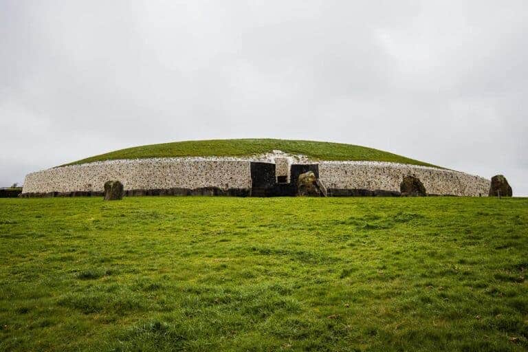 The ancient Newgrange passage tomb in Ireland, a large circular stone structure with a grassy dome, set against an overcast sky.