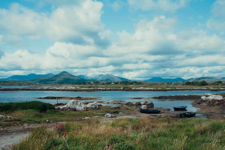 A panoramic view of Connemara, Ireland, featuring a winding lake bordered by grassy and rocky terrain, with majestic mountains in the distance.