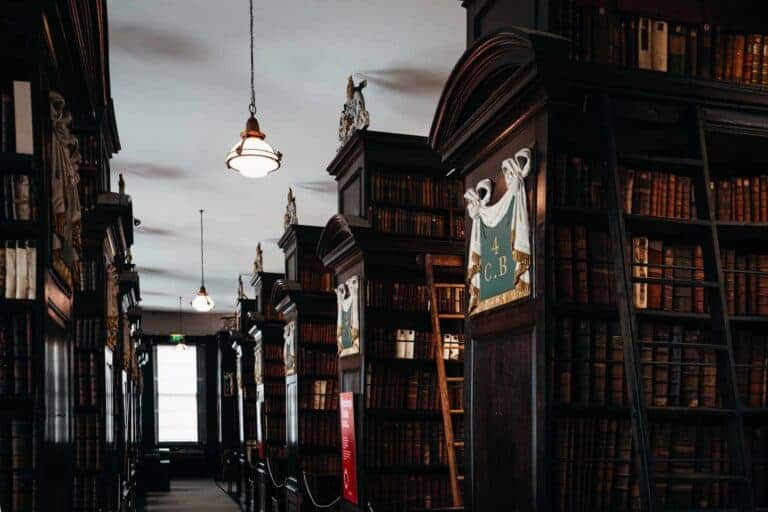 A long, dimly lit hallway in Marsh's Library, lined with towering bookshelves and hanging lanterns. The grand space exudes historical charm.