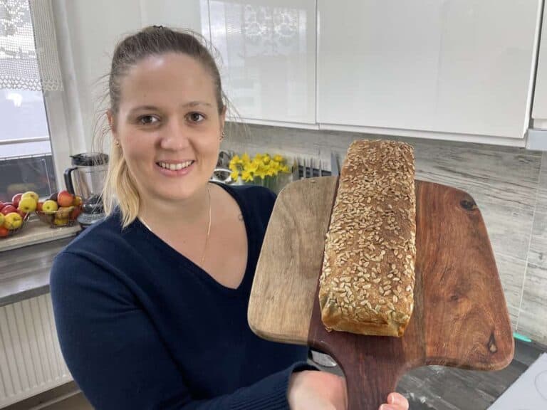 Woman presenting a freshly baked Polish sunflower seed bread in the kitchen.